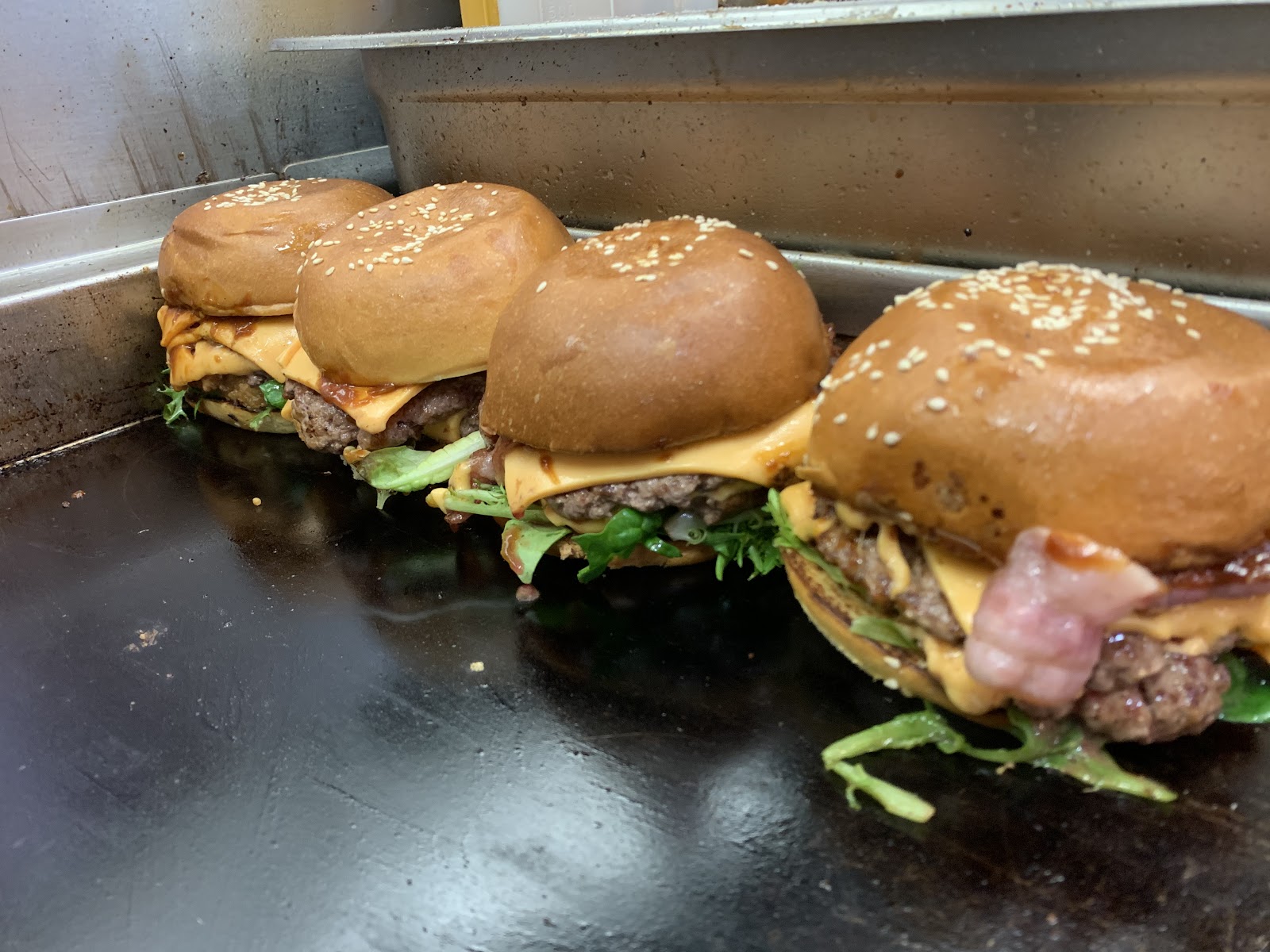 Four burgers with melted cheese and bacon on the flat-top grill at Feast